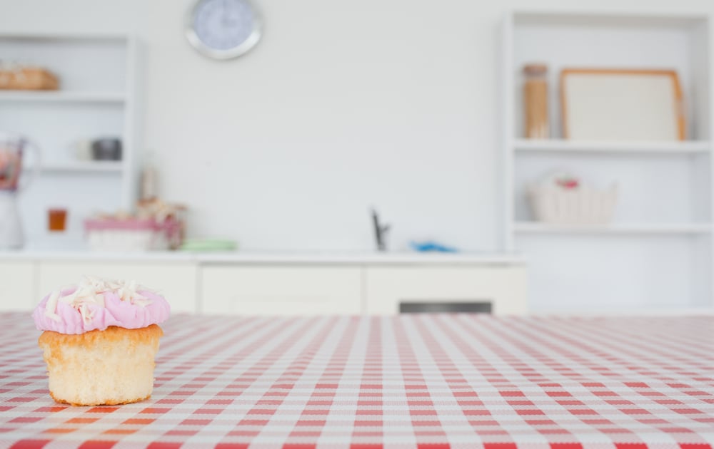 A cupcake on a tablecloth in a kitchen