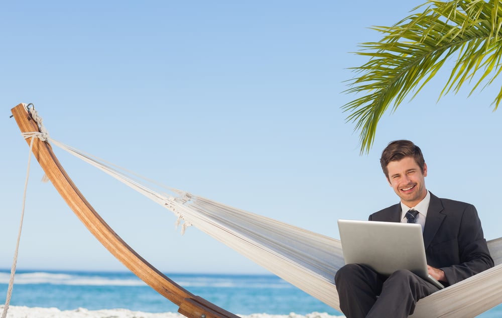 Businessman sitting in hammock using laptop looking at camera on beach