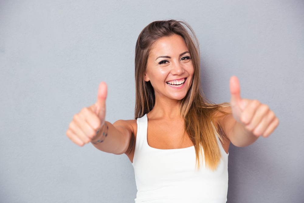 Cheerful lovely girl showing thumbs up over gray background. Looking at camera