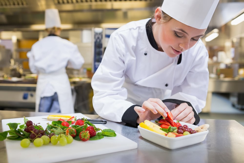 Chef putting a strawberry in the fruit salad in the kitchen