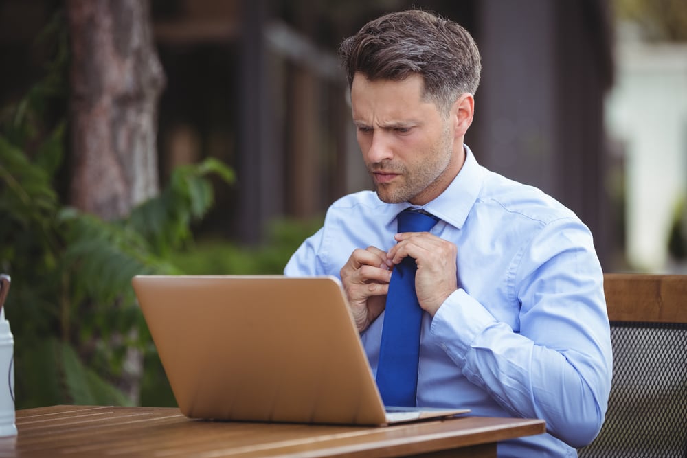 Handsome businessman adjusting tie while using laptop at outdoor