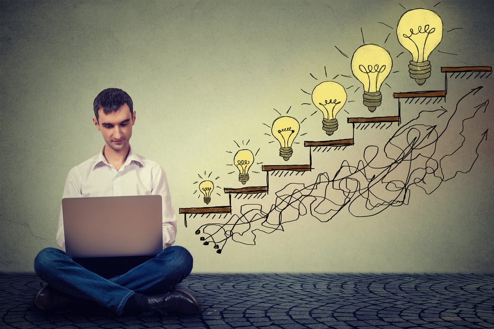 Happy young man entrepreneur working on computer sitting on a floor in his office successful in increasing internet website traffic. Promotion, company growth concept. Isolated on gray wall background