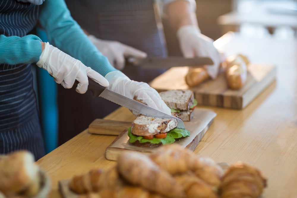 Mid-section of waiter chopping bread roll and sandwich on chopping board in cafx92xA9