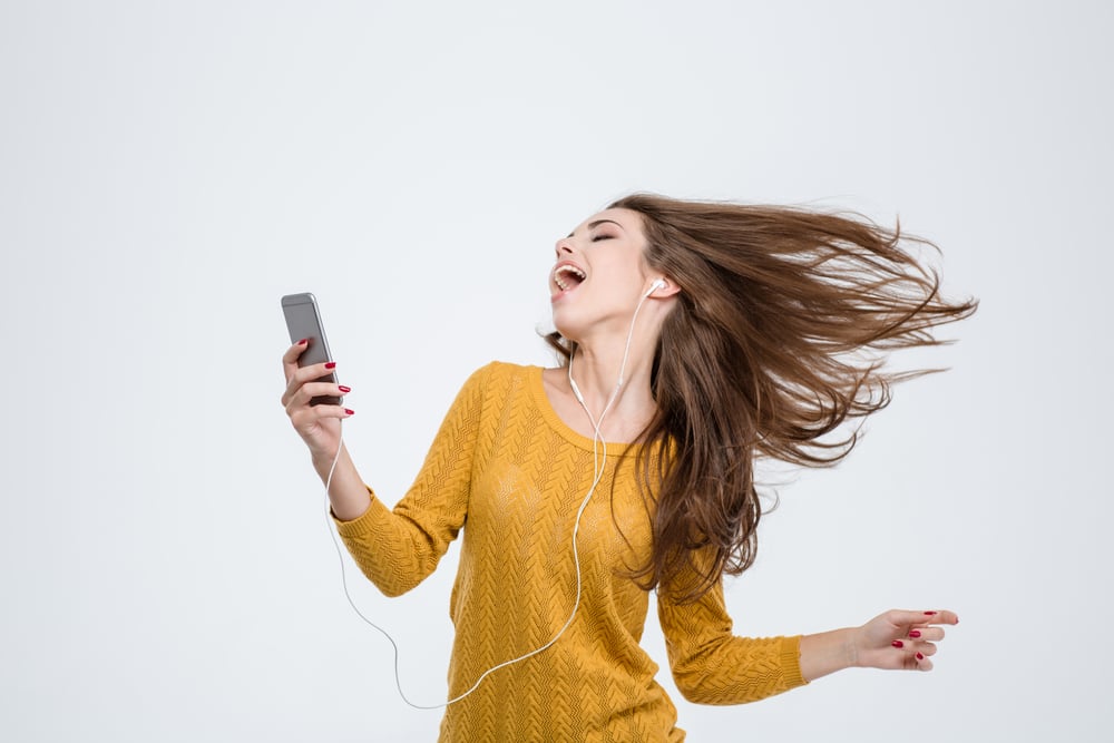 Portrait of a cheerful cute woman listening music in headphones and dancing isolated on a white background