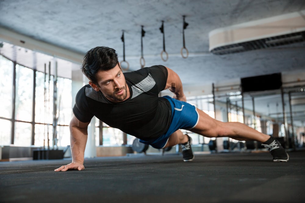 Portrait of a handsome man doing push ups exercise with one hand in fitness gym