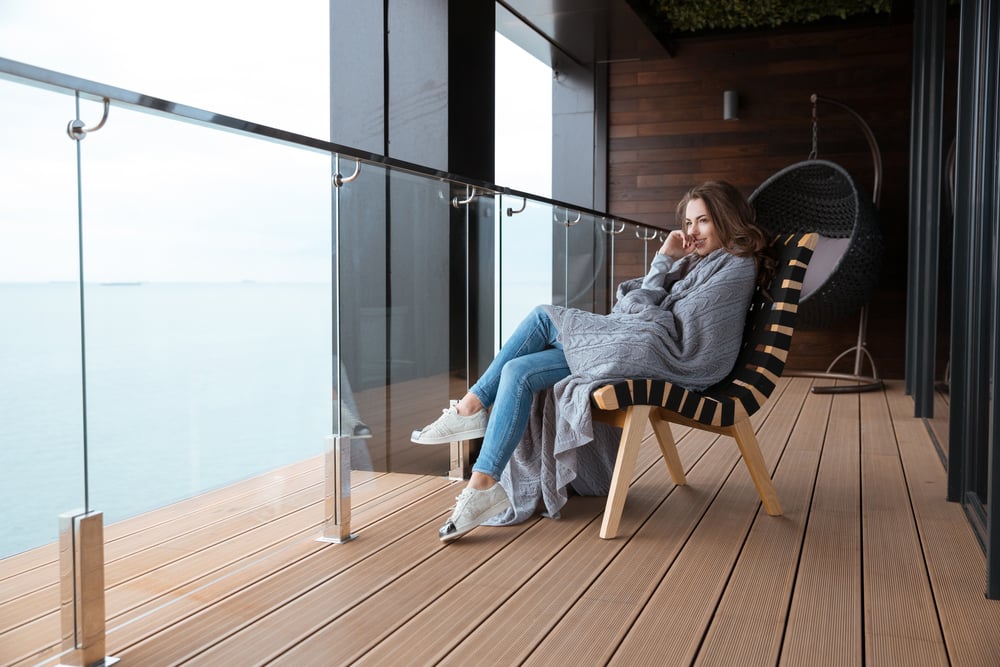 Smiling young woman sitting wrapped in knitted coverlet on the glass balcony-1