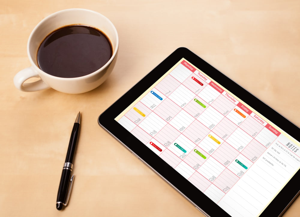 Workplace with tablet pc showing calendar and a cup of coffee on a wooden work table close-up-3