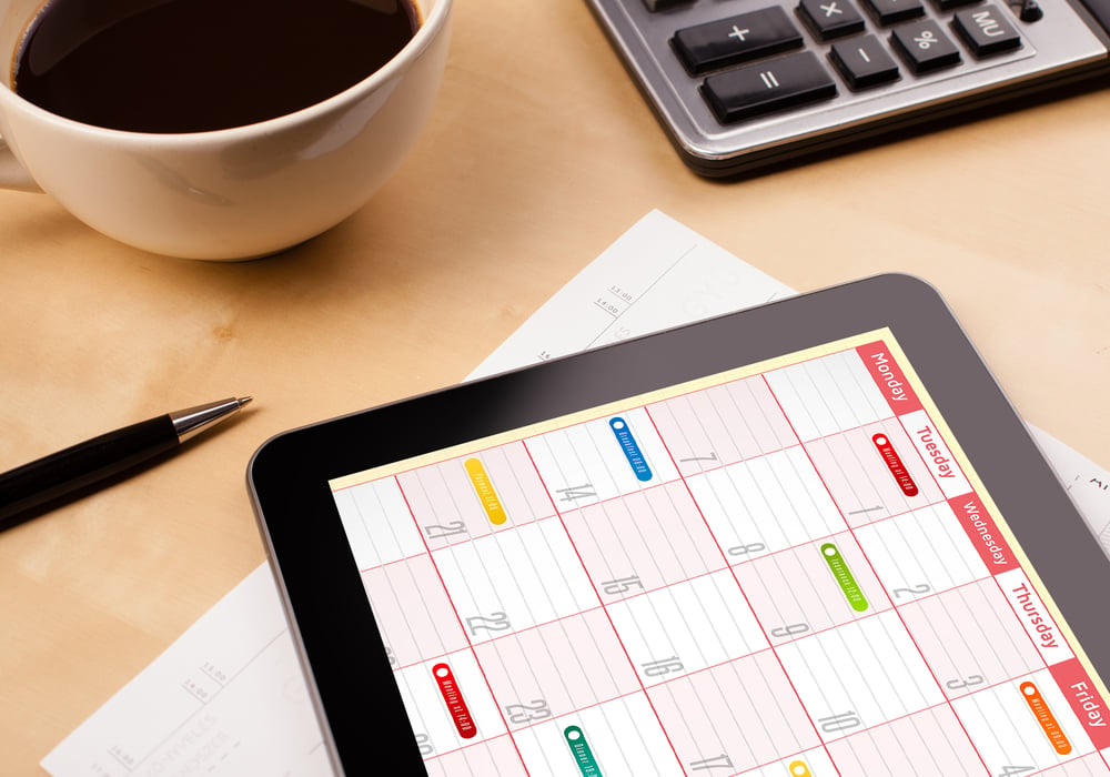 Workplace with tablet pc showing calendar and a cup of coffee on a wooden work table close-up-Oct-04-2023-03-28-43-3319-PM